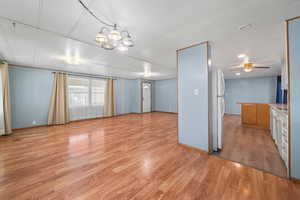 Interior space featuring baseboards, light wood-type flooring, and ceiling fan with notable chandelier