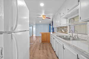 Kitchen featuring a ceiling fan, white appliances, a sink, light wood-style floors, and white cabinets