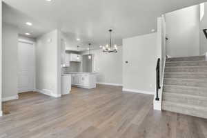 Unfurnished living room featuring a chandelier, stairs, recessed lighting, light wood-type flooring, and baseboards