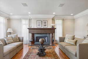 Living room featuring visible vents, wood finished floors, a fireplace with raised hearth, and ornamental molding