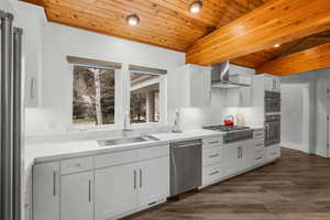 Kitchen featuring wood ceiling, a sink, wall chimney exhaust hood, vaulted ceiling, and appliances with stainless steel finishes