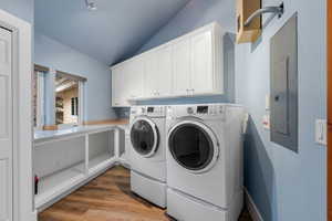 Washroom featuring washer and clothes dryer, electric panel, cabinet space, and wood finished floors
