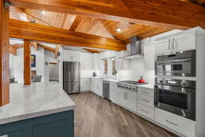 Kitchen with wood ceiling, a sink, lofted ceiling with beams, wall chimney range hood, and appliances with stainless steel finishes