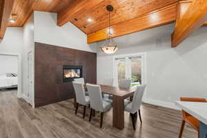 Dining space featuring wood finished floors, beam ceiling, high vaulted ceiling, visible vents, and a tiled fireplace