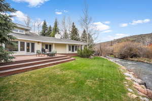 Back of house featuring a wooden deck, french doors, a chimney, and a lawn