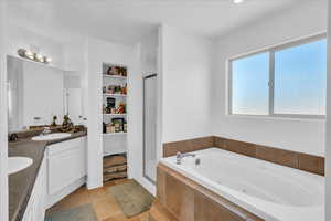 Full bathroom featuring double vanity, a jetted tub, a stall shower, and a sink