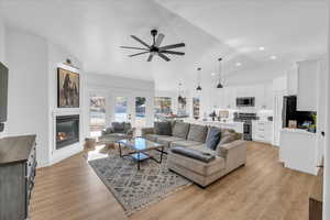 Living room with light wood finished floors, a ceiling fan, a glass covered fireplace, lofted ceiling, and recessed lighting