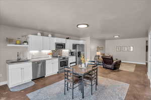 Kitchen with a sink, open shelves, white cabinets, baseboards, and appliances with stainless steel finishes