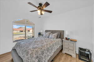 Bedroom with light wood-type flooring, baseboards, heating unit, and a ceiling fan