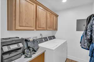 Laundry room with electric panel, cabinet space, wood finished floors, washing machine and clothes dryer, and baseboards