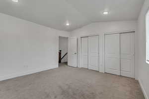 Unfurnished bedroom featuring carpet flooring, vaulted ceiling, baseboards, and multiple closets