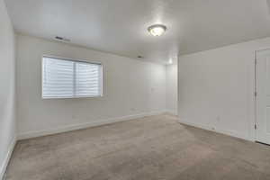 Spare room with light carpet, a textured ceiling, baseboards, and visible vents