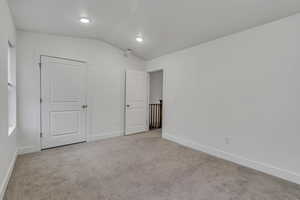 Unfurnished bedroom featuring vaulted ceiling, light carpet, and baseboards