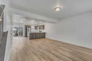 Unfurnished living room featuring light wood-style floors, baseboards, a sink, and recessed lighting
