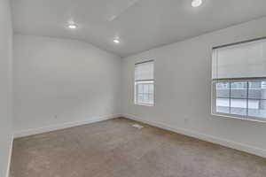 Carpeted spare room with baseboards, visible vents, recessed lighting, and vaulted ceiling