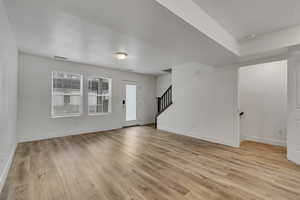 Unfurnished living room with light wood-style flooring, stairs, baseboards, and visible vents