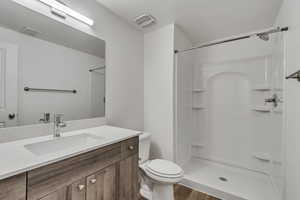 Bathroom featuring toilet, a shower, wood finished floors, and vanity