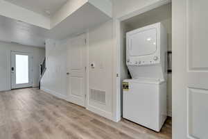 Washroom with stacked washer and clothes dryer, baseboards, visible vents, and light wood-style floors