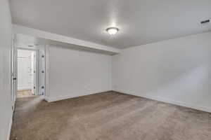 Carpeted spare room with baseboards, visible vents, and a textured ceiling