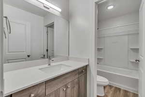 Full bath with shower / bath combination, vanity, toilet, and wood finished floors