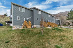 Back of house with a mountain view, a lawn, and central AC