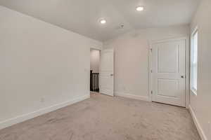 Unfurnished bedroom with vaulted ceiling, light carpet, and baseboards