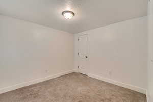 Empty room featuring baseboards, a textured ceiling, and light colored carpet