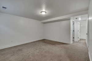 Finished below grade area featuring baseboards, a textured ceiling, and carpet