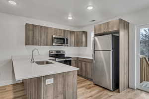 Kitchen with a sink, a peninsula, light wood-style flooring, light countertops, and appliances with stainless steel finishes