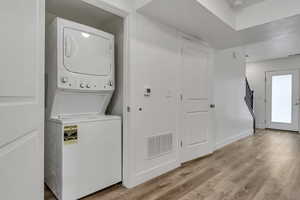 Washroom featuring baseboards, light wood finished floors, visible vents, laundry area, and stacked washer / drying machine