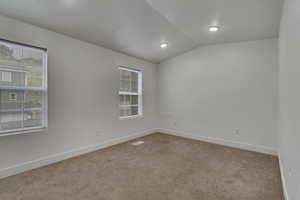 Carpeted spare room with lofted ceiling, a wealth of natural light, baseboards, and visible vents