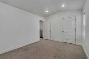 Unfurnished bedroom with lofted ceiling, baseboards, and light colored carpet