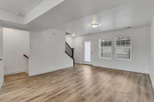 Unfurnished living room with visible vents, baseboards, light wood-style flooring, and stairs