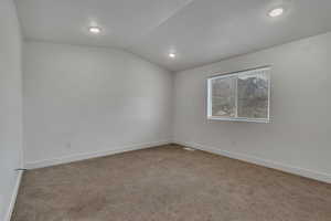 Carpeted spare room featuring vaulted ceiling, baseboards, and recessed lighting