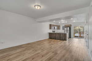 Kitchen with appliances with stainless steel finishes, open floor plan, a peninsula, light countertops, and light wood-type flooring