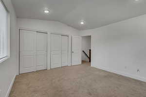 Unfurnished bedroom featuring carpet flooring, baseboards, lofted ceiling, and multiple closets