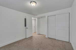 Unfurnished bedroom with a textured ceiling, carpet floors, baseboards, and a closet