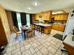 Kitchen with a peninsula, stainless steel appliances, a textured ceiling, a kitchen bar, and light countertops