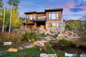 Back of property featuring a balcony, stone siding, a chimney, and a small pond