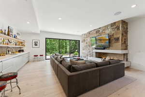 Living room featuring a stone fireplace, light wood-style flooring, recessed lighting, and wet bar