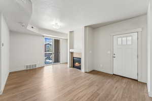 Unfurnished living room with a tiled fireplace, visible vents, light wood-style flooring, and a textured ceiling