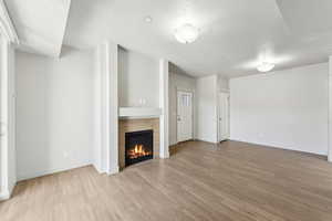 Unfurnished living room featuring light wood finished floors, a textured ceiling, a tiled fireplace, and baseboards