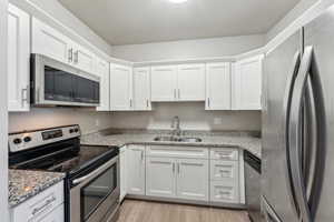 Kitchen featuring light stone countertops, light wood-style flooring, a sink, white cabinetry, and appliances with stainless steel finishes