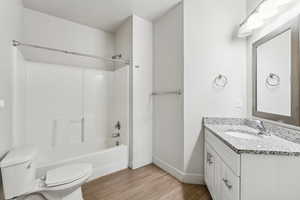 Full bath with shower / bath combination, toilet, baseboards, vanity, and wood finished floors