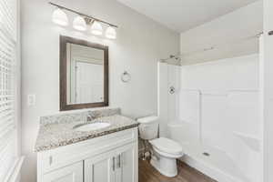 Bathroom featuring toilet, a shower, wood finished floors, and vanity