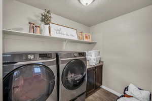 Laundry area with cabinet space, a textured ceiling, dark wood-type flooring, baseboards, and independent washer and dryer
