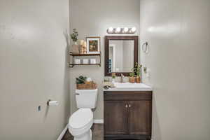 Half bathroom with toilet, baseboards, and vanity