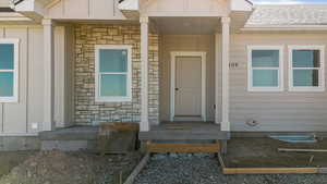 Property entrance with stone siding, a shingled roof, and board and batten siding