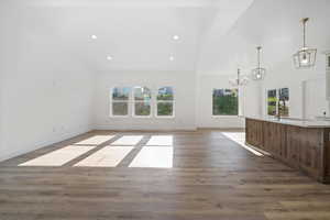 Unfurnished living room featuring an inviting chandelier, high vaulted ceiling, plenty of natural light, and wood finished floors