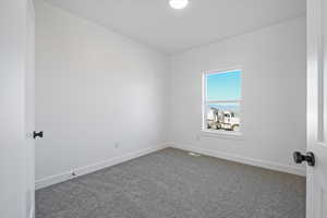 Empty room featuring baseboards, dark colored carpet, and visible vents
